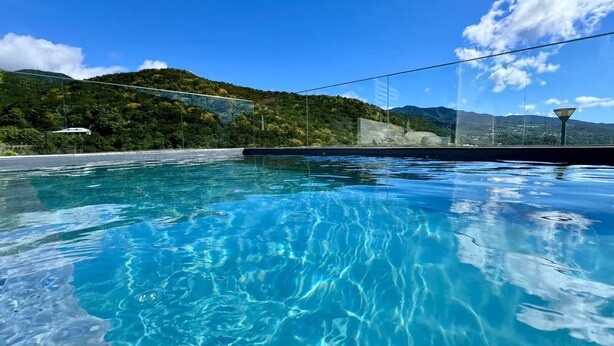 A swimming pool with clear blue water, surrounded by lush greenery and mountains in the background.