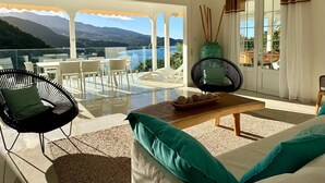 A balcony with a view of mountains and a pool, furnished with chairs and a table.