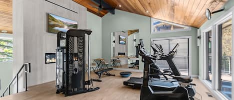 A modern gym with cardio equipment, a weight machine, and a fireplace.
