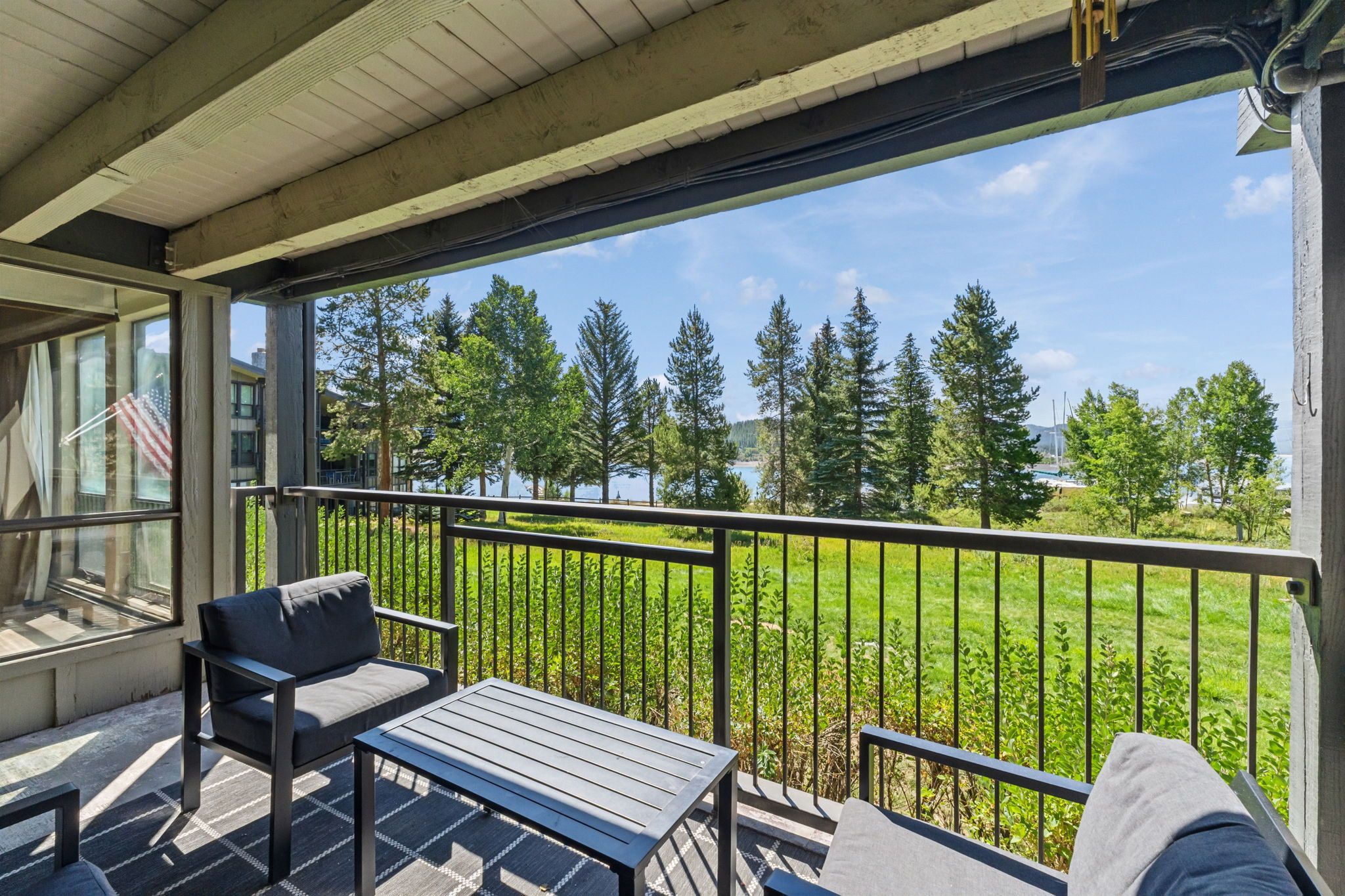 A balcony with a view of a lake and trees, a table, and a chair.