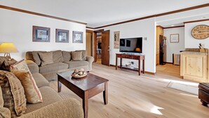 A living room with a sofa, coffee table, and television. There is a wooden cabinet and a clock on the wall. - Stunning 2BR on Lake Dillon w/ Pool and Concert Access! (Dillon)
