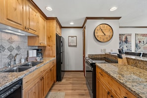 A kitchen with wooden cabinets, granite countertops, a stainless steel refrigerator, and a wall clock. - Stunning 2BR on Lake Dillon w/ Pool and Concert Access! (Dillon)