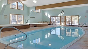 An indoor swimming pool with clear glass walls, a lounge area with chairs, and a view of the outside. - Stunning 2BR on Lake Dillon w/ Pool and Concert Access! (Dillon)