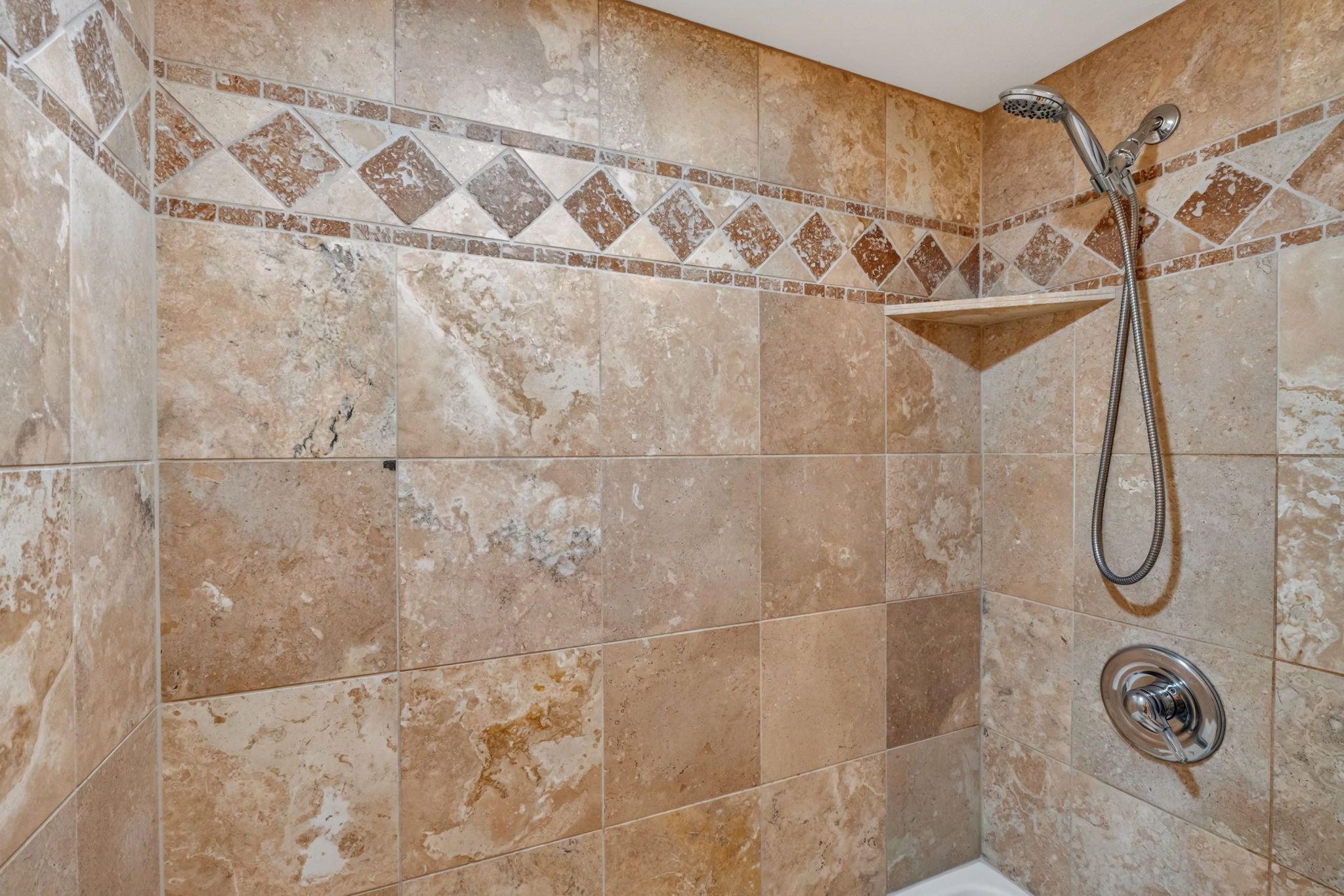 A shower area with a handheld showerhead and a wall-mounted faucet.