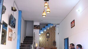 A reception area with a staircase, wooden reception desk, and two people sitting on a bench. - All In One Guest House (Bareilly)