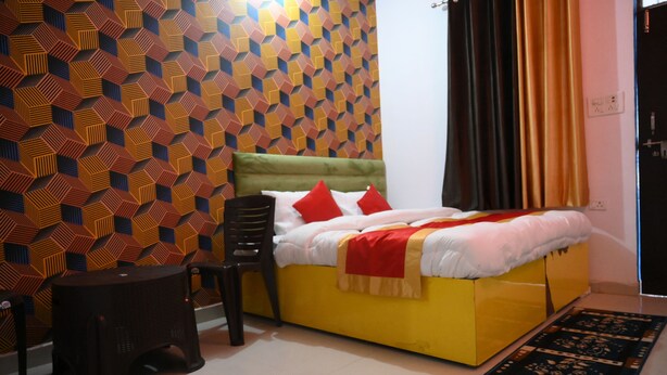 A room with a geometric patterned wall, a bed with red and white bedding, a green upholstered headboard, and a small stool. - All In One Guest House (Bareilly)