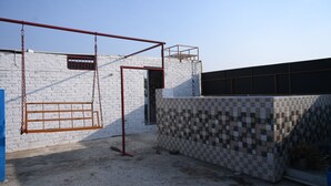 A building with a white brick exterior, a metal gate, and a tiled wall. - All In One Guest House (Bareilly)