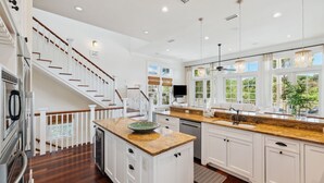 A modern kitchen with white cabinetry, a wooden staircase, and a large window offering a view of greenery.