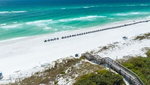 A beach with a wooden walkway leading to a sandy area, a row of beach umbrellas, and a clear view of the ocean.