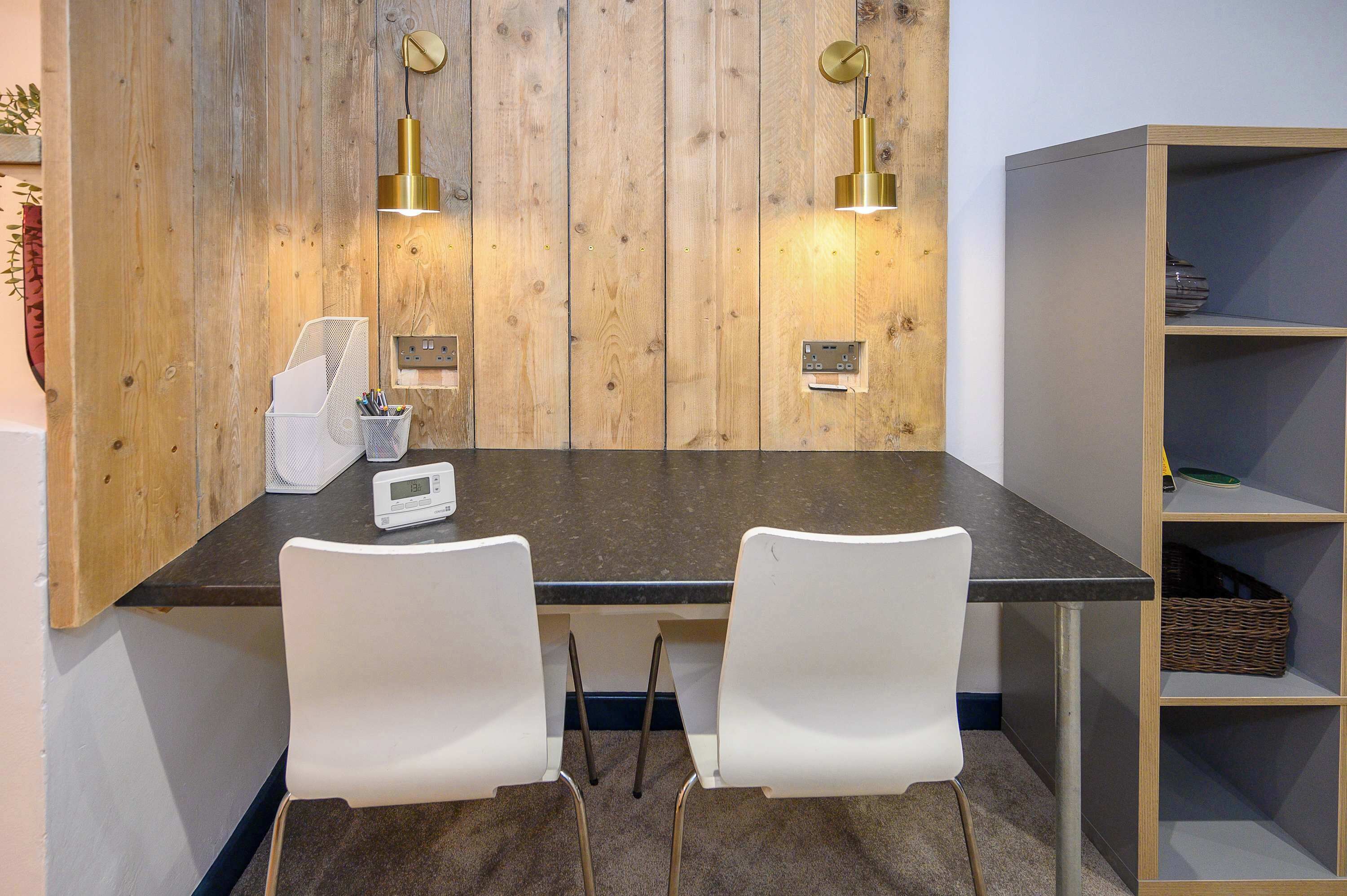Un espace de bureau moderne avec un mur en bois, deux chaises blanches, un bureau, une bibliothèque et deux lampes suspendues.