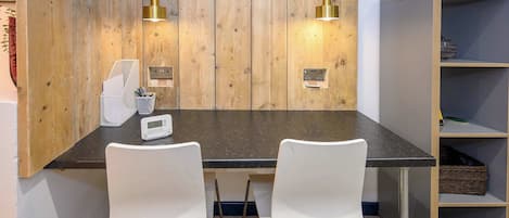Ein moderner Arbeitsraum mit einer Holzvertäfelung, zwei weißen Stühlen, einem Schreibtisch, einem Bücherregal und zwei Pendelleuchten.