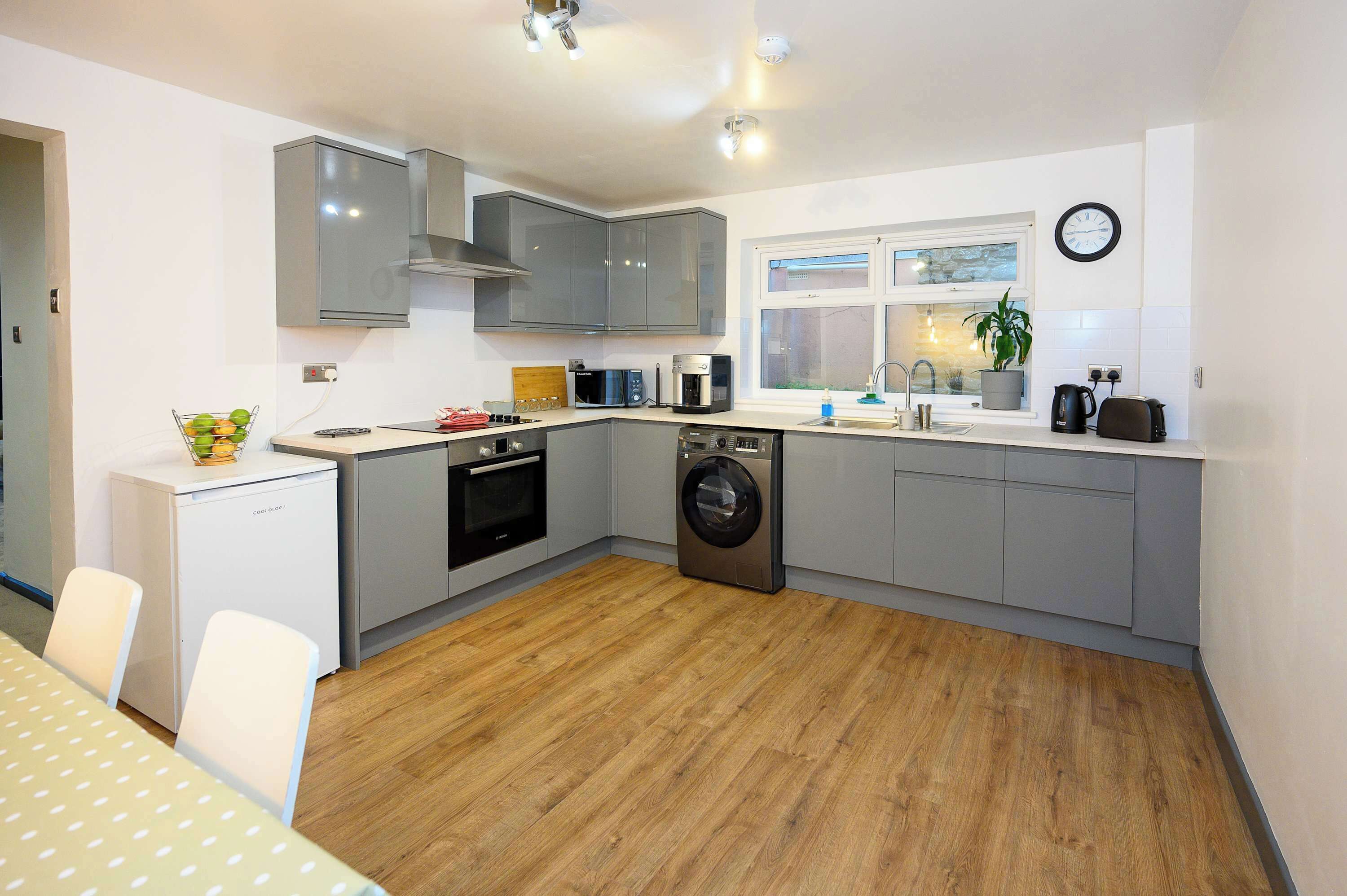 A compact kitchen with grey cabinets, a built-in oven, microwave, and washing machine.