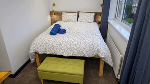 Een net opgemaakt bed met bloemenbedekking, een groene bank en een raam met gordijnen.