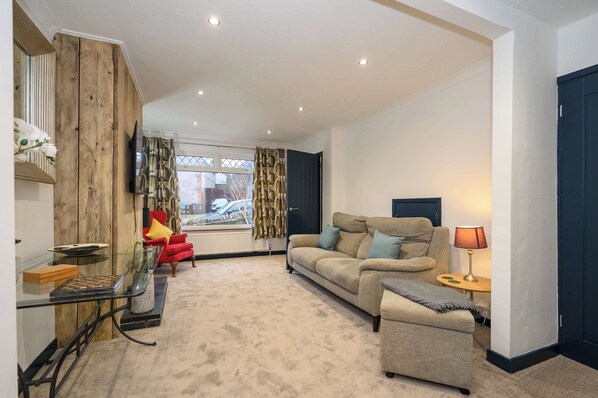 A living room with a sofa, armchair, and a glass coffee table.