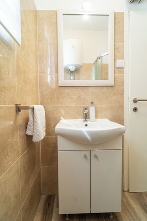 A bathroom with beige tiles, a white sink, a mirror, and a towel rack. - Zadar Leisure Suites (Zadar)