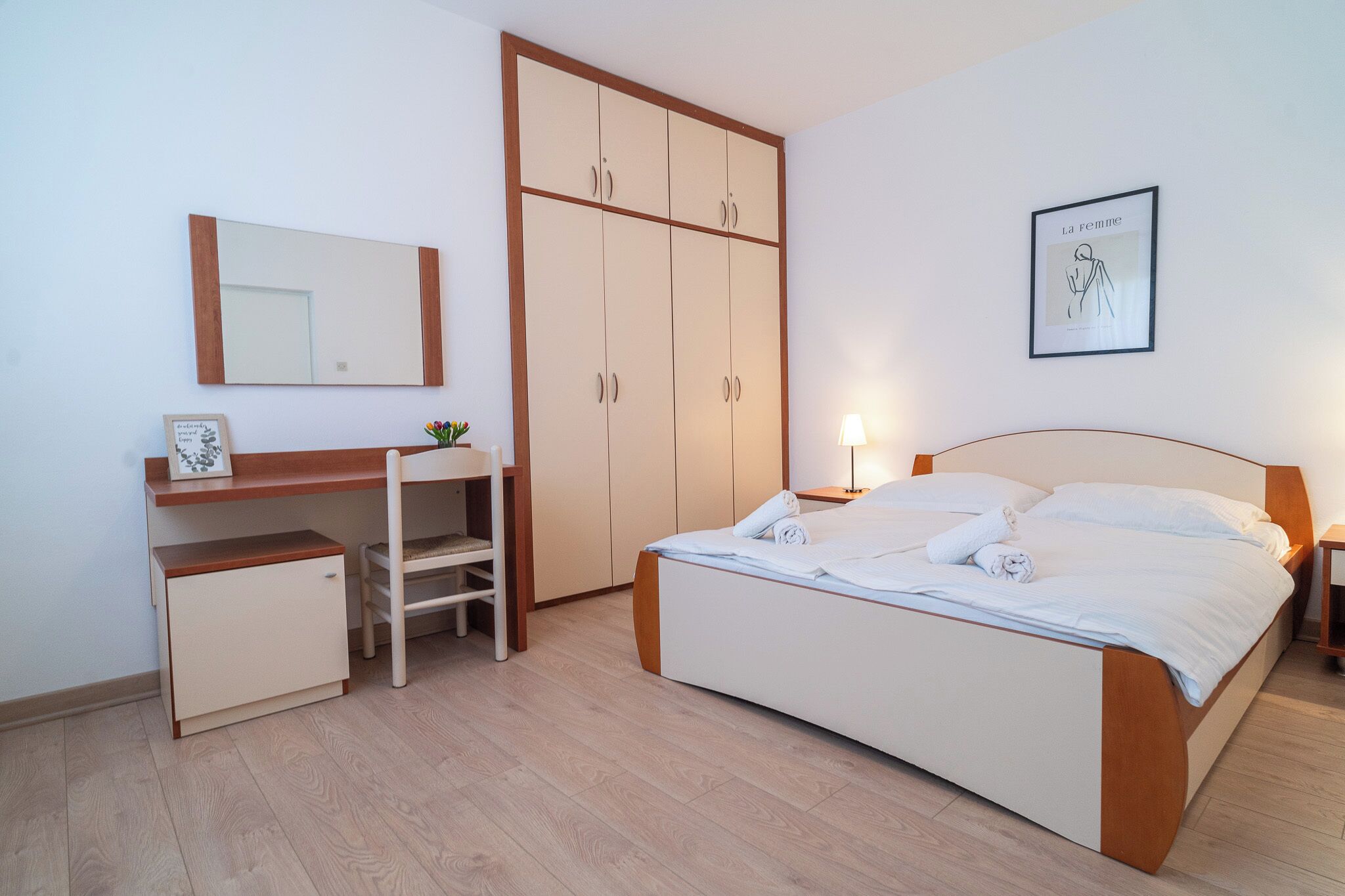 A bedroom with a bed, a desk, a wardrobe, a mirror, and a framed picture on the wall.