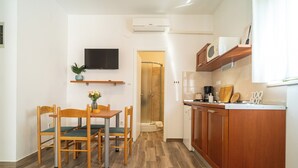 Een kleine keuken met houten kastjes, een ingebouwde magnetron en een eethoekje met een tafel en stoelen.
