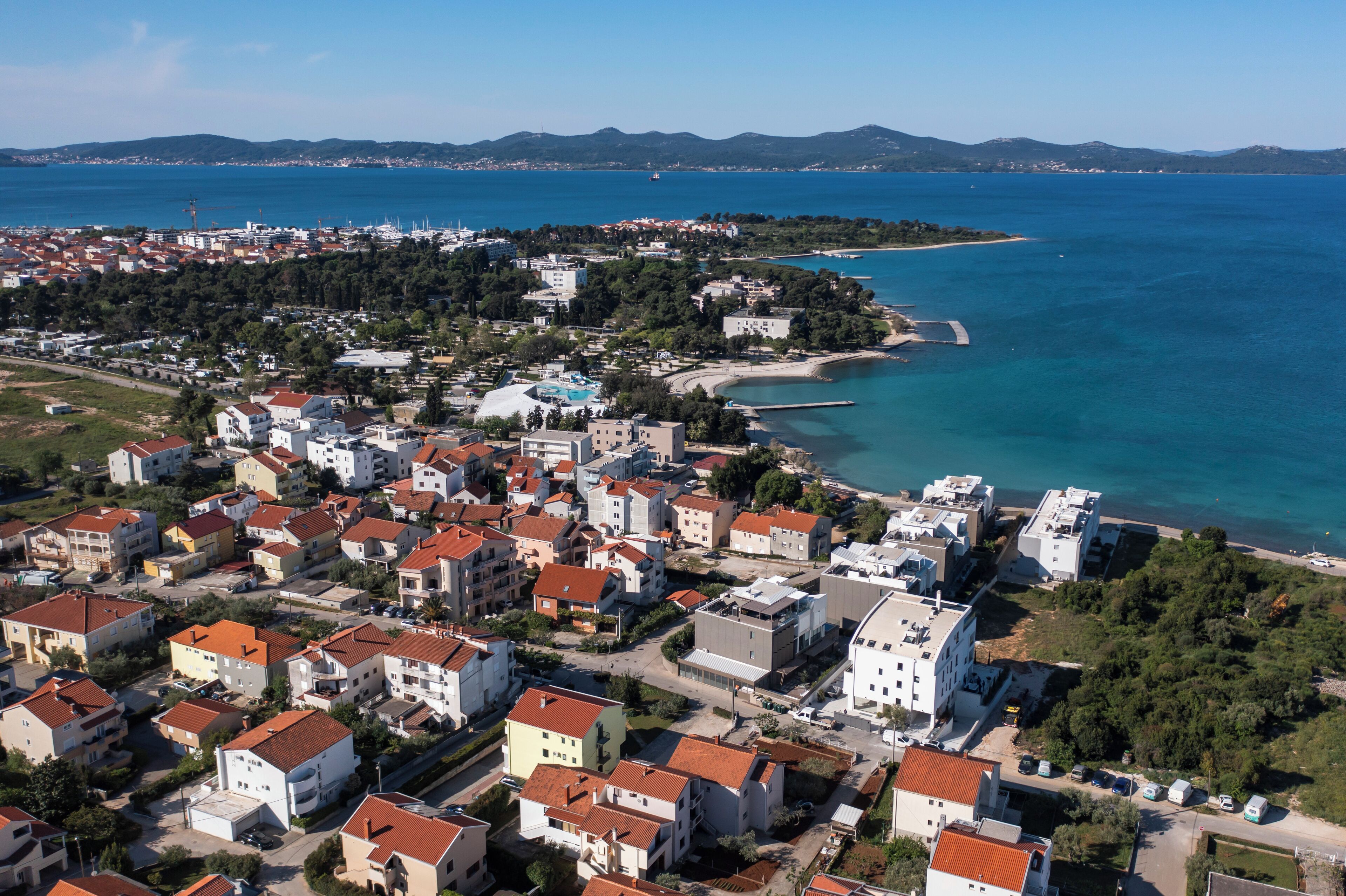 An aerial view of a coastal town with residential buildings, a beach, and a clear blue sea.