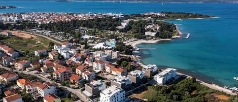An aerial view of a coastal town with residential buildings, a beach, and a clear blue sea.