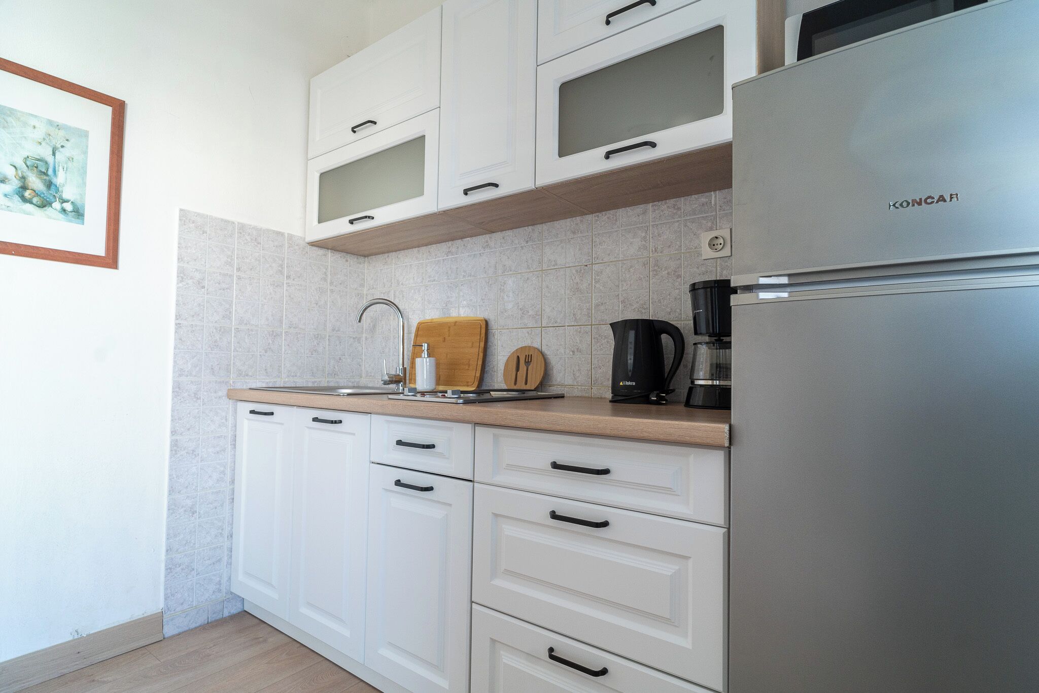A modern kitchen with white cabinets, a stainless steel refrigerator, and a coffee maker.