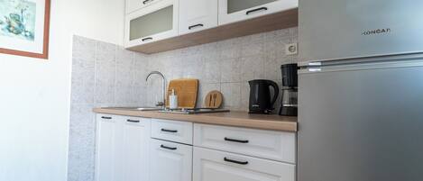 A modern kitchen with white cabinets, a stainless steel refrigerator, and a coffee maker.