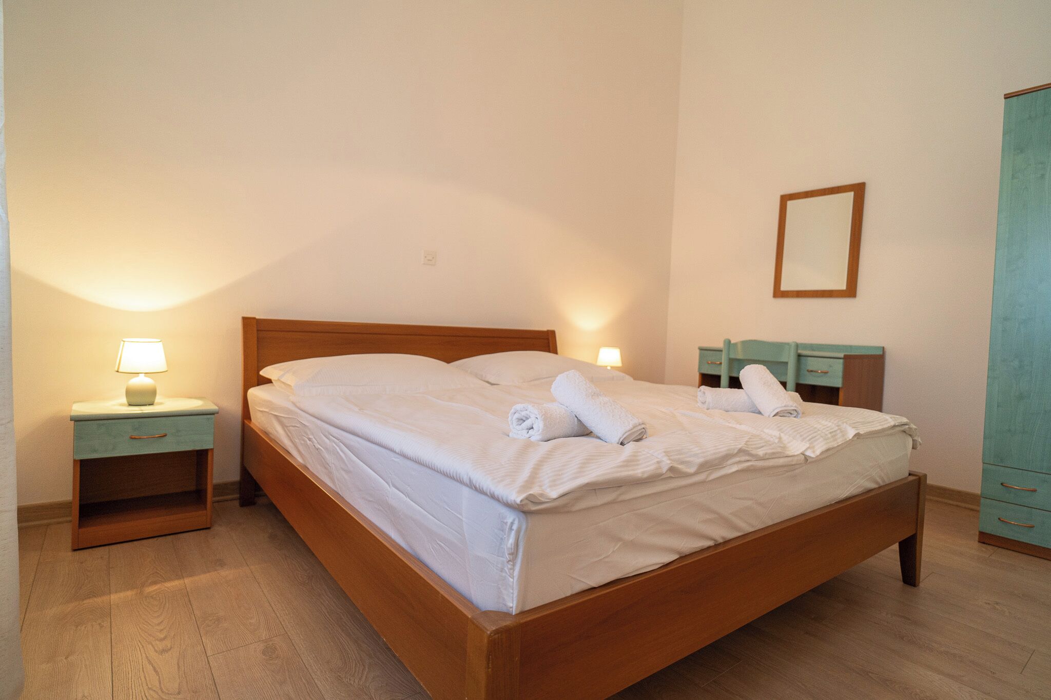 A neatly made bed with white linens and towels, a wooden headboard, and a nightstand with a lamp.