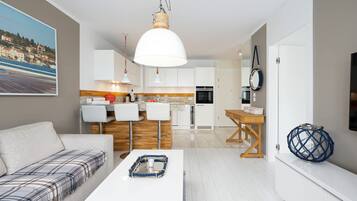Una sala moderna con un sofá, una mesa de centro y una zona de cocina con armarios blancos y una lámpara colgante.