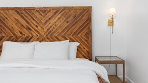 Ein Bett mit hölzernem Kopfteil, ein Nachttisch und eine Wandleuchte.
