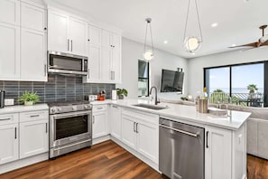 A modern kitchen with white cabinets, stainless steel appliances, a large window with a view, and a ceiling fan. - Blue Pearl 5BR Home with Private Pool (Indian Shores)
