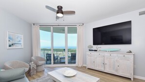 A modern living room with a sofa, a coffee table, a TV, a cabinet, and a view through the glass door. - Condo in the heart of Destin! Lagoon-style pool and tons of great amenities! (Destin)