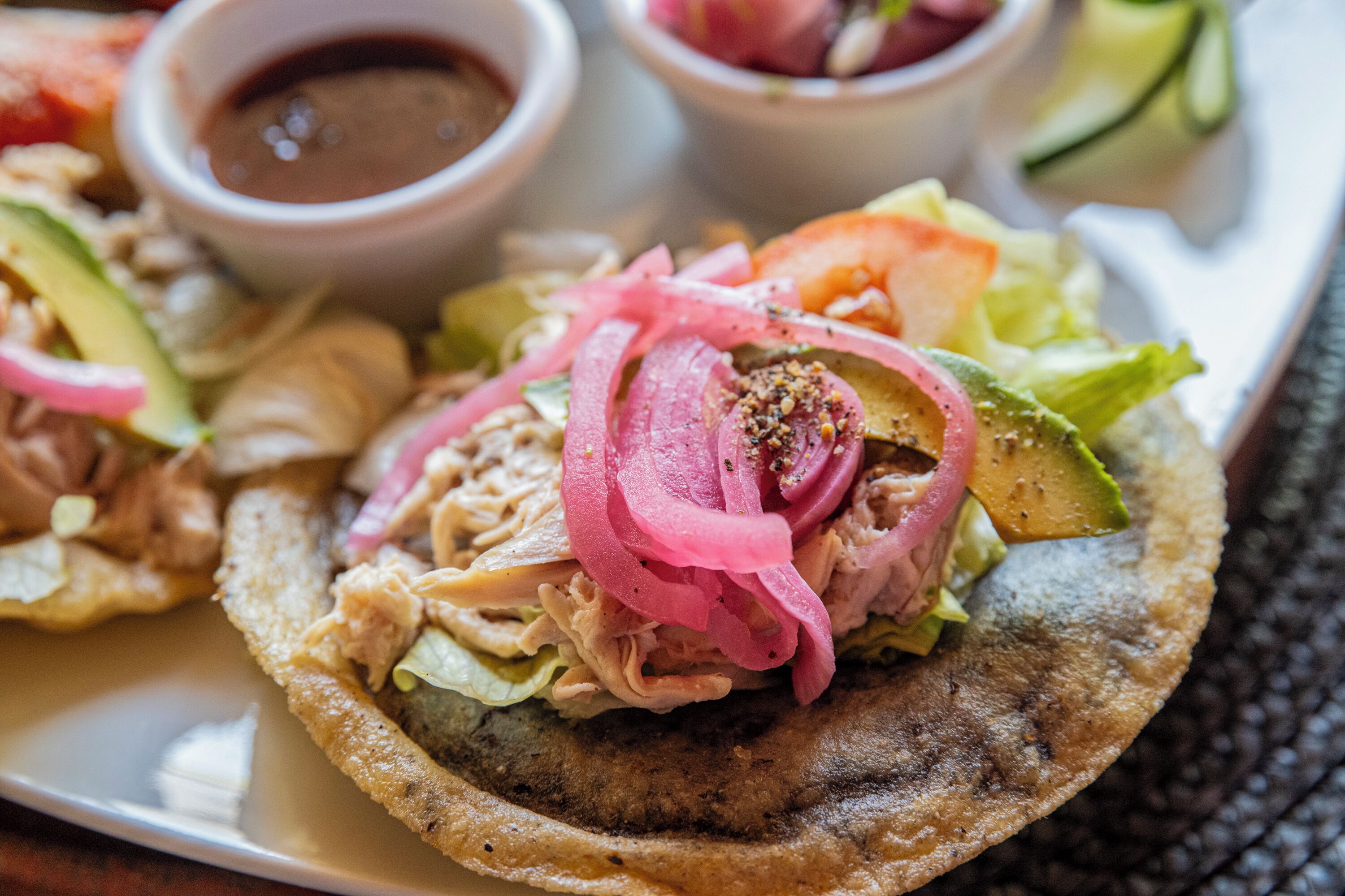 A plate with a food item, possibly a taco, with toppings like lettuce, avocado, and a pink sauce.