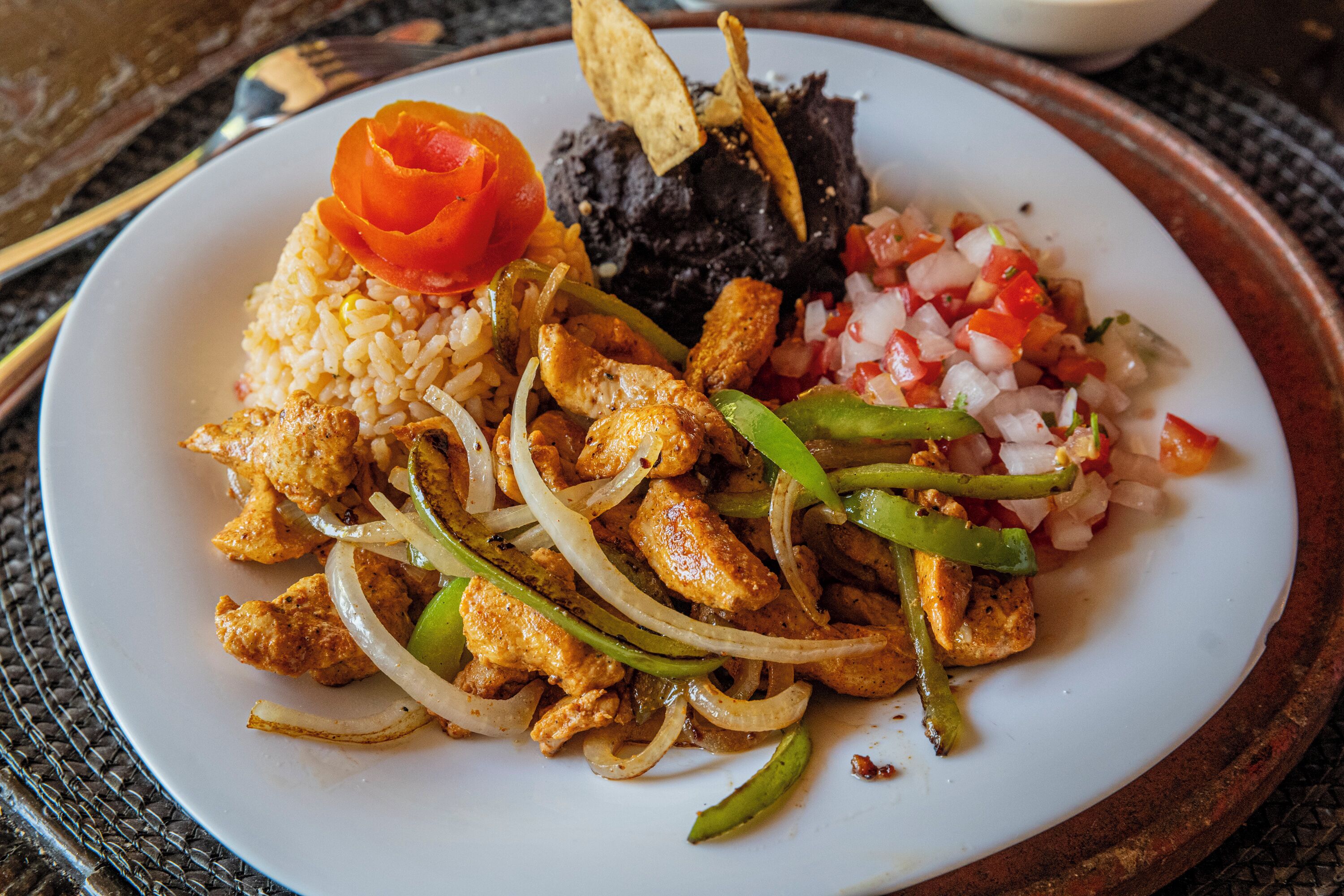 Un plato de comida con arroz, frijoles negros, pollo, cebollas y pimientos.