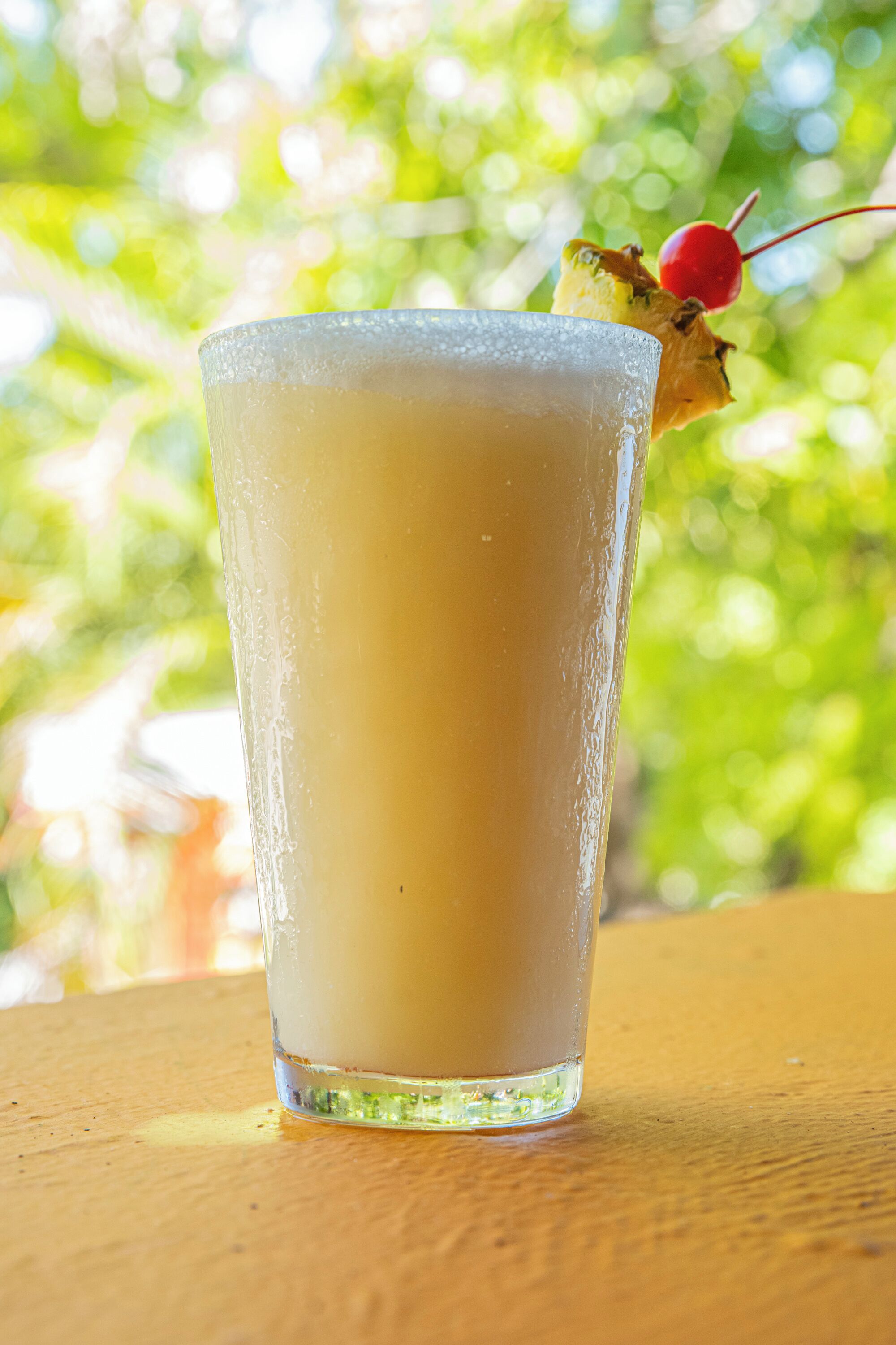 A tall glass with a frothy beverage, a cherry garnish, and a blurred green background.