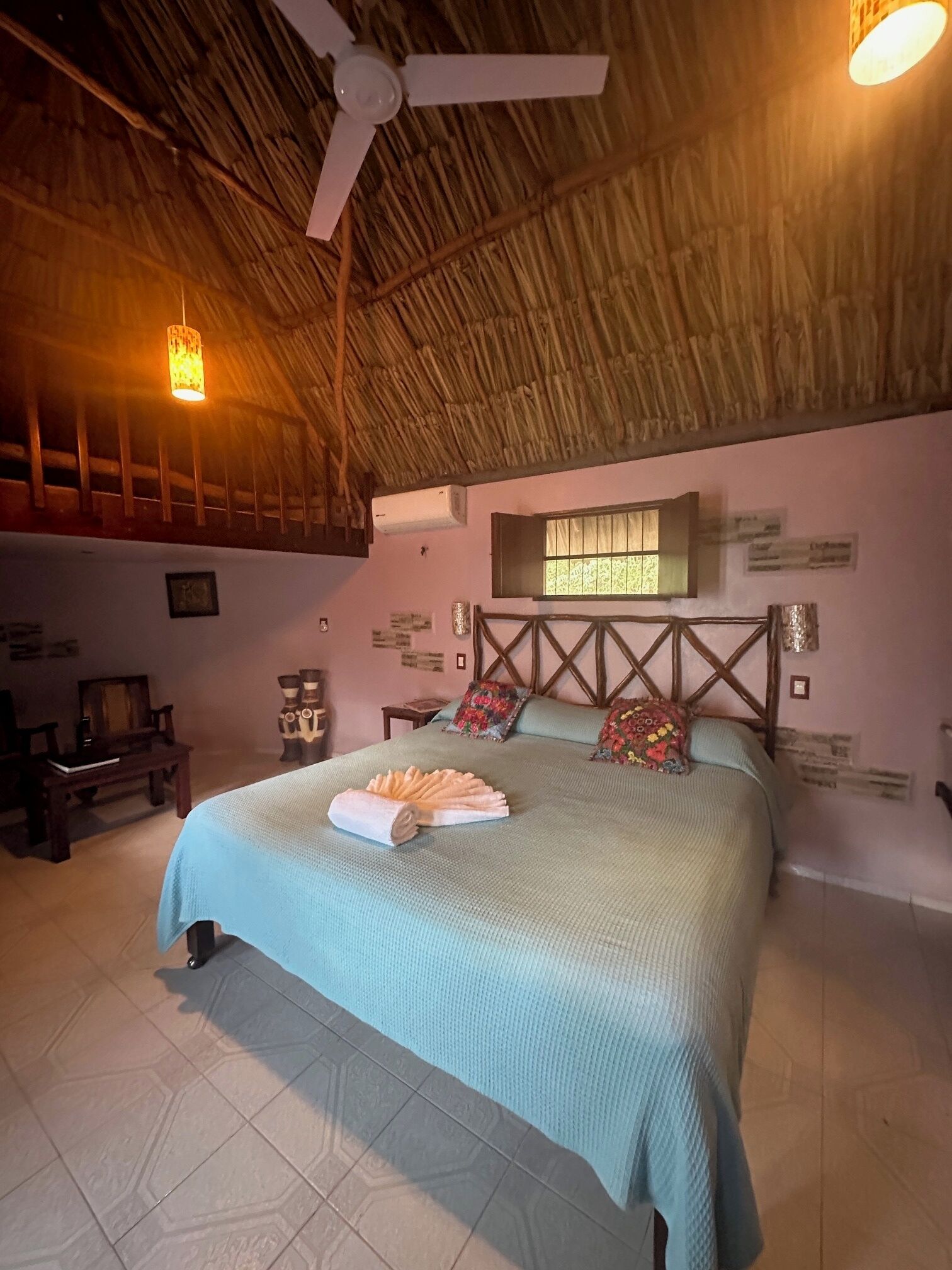 Una habitación con cama, ventilador de techo, ventana y aire acondicionado instalado en la pared.