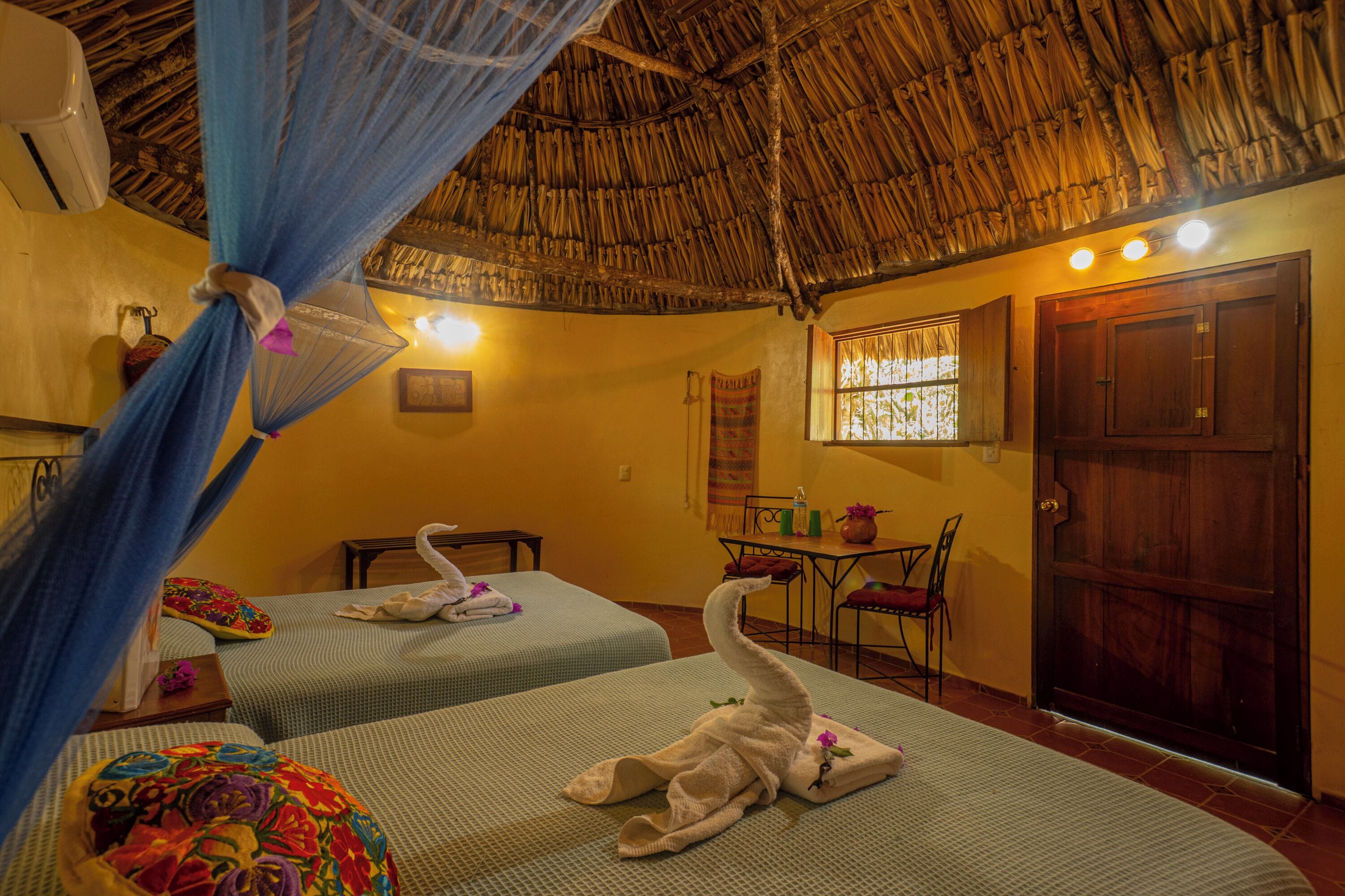 A room with two beds, a thatched roof, a wooden door, and a small table with chairs.