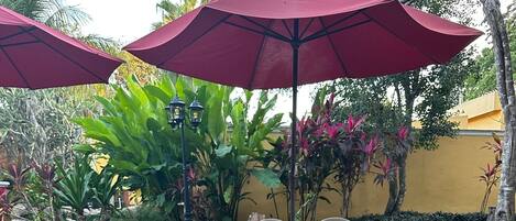 A garden area with a stone fountain surrounded by pebbles, outdoor seating, and red umbrellas.