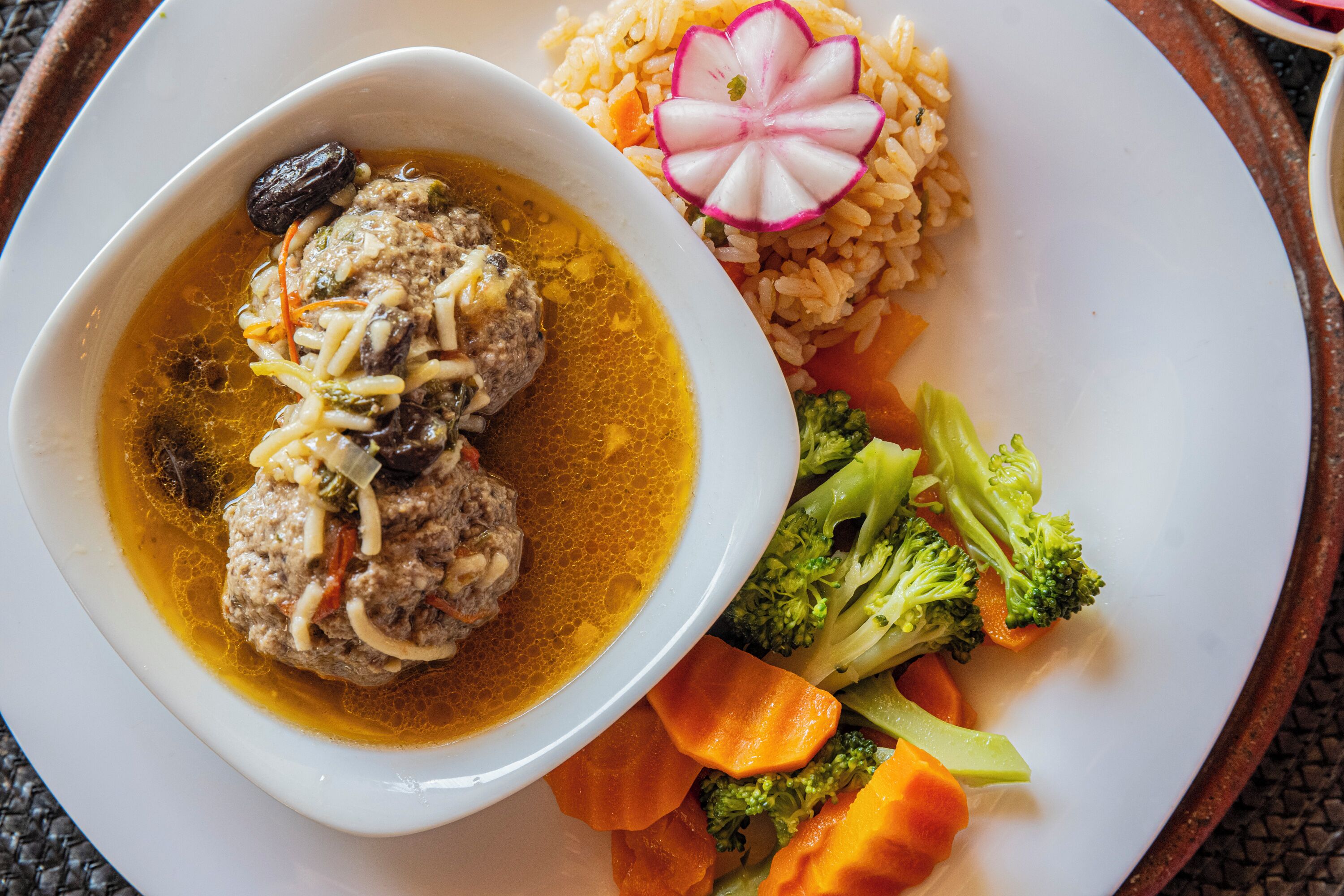 A plate with meatballs in a yellow sauce, rice, and vegetables.