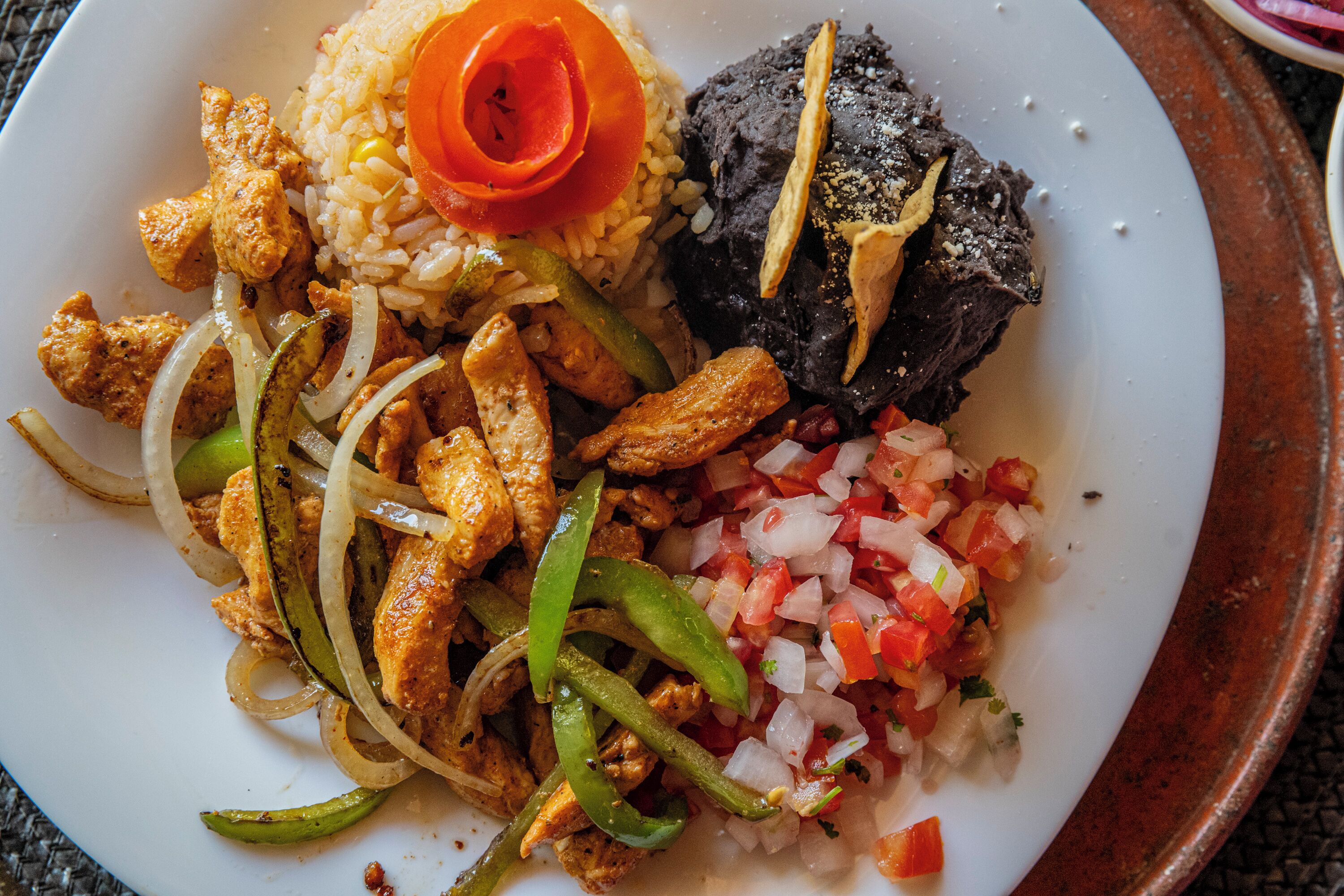 Ein Teller Essen mit Reis, Hähnchen, Zwiebeln, Paprika und einer Tomaten-Salsa.