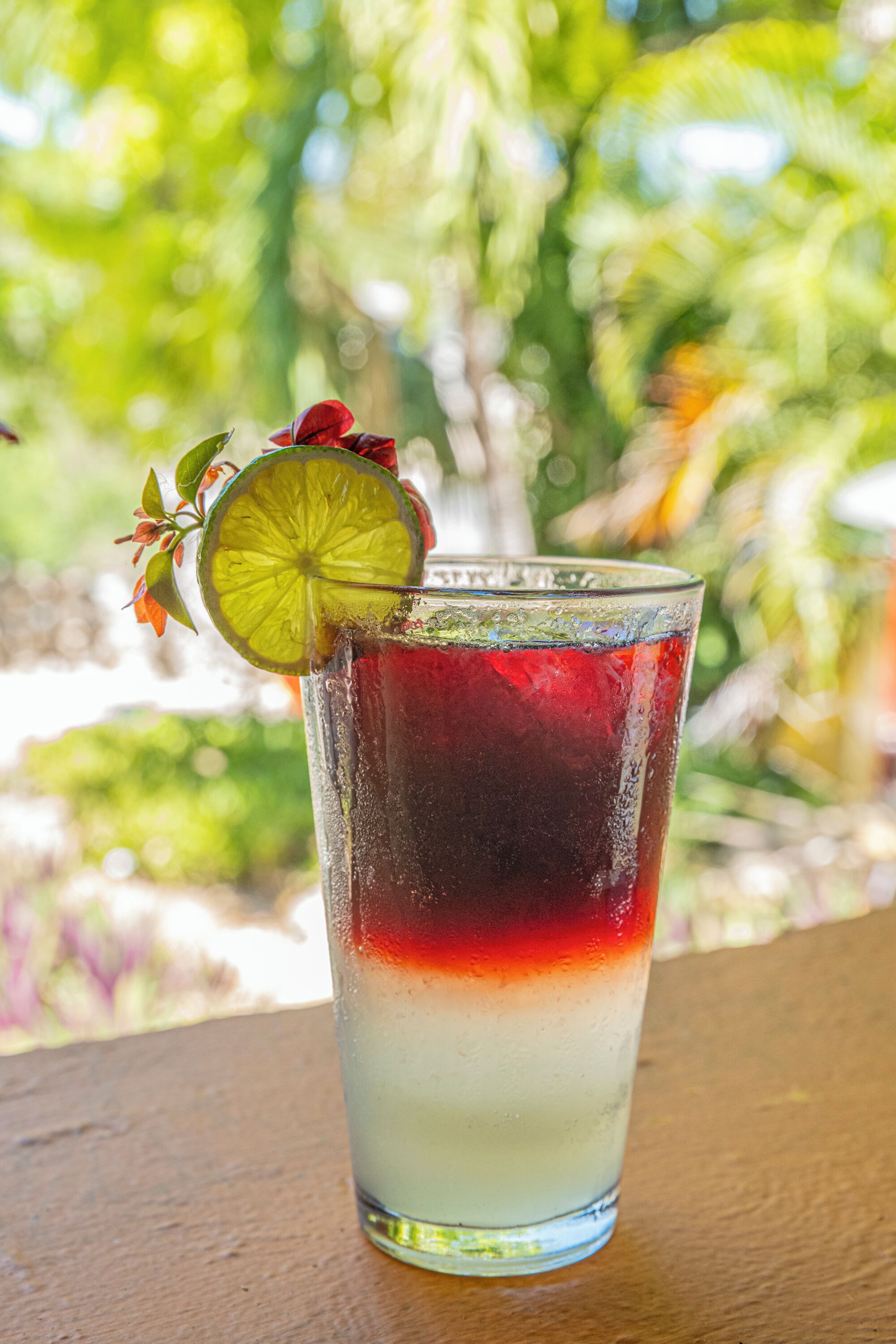 A glass with layered drinks and a lime garnish on a wooden surface.