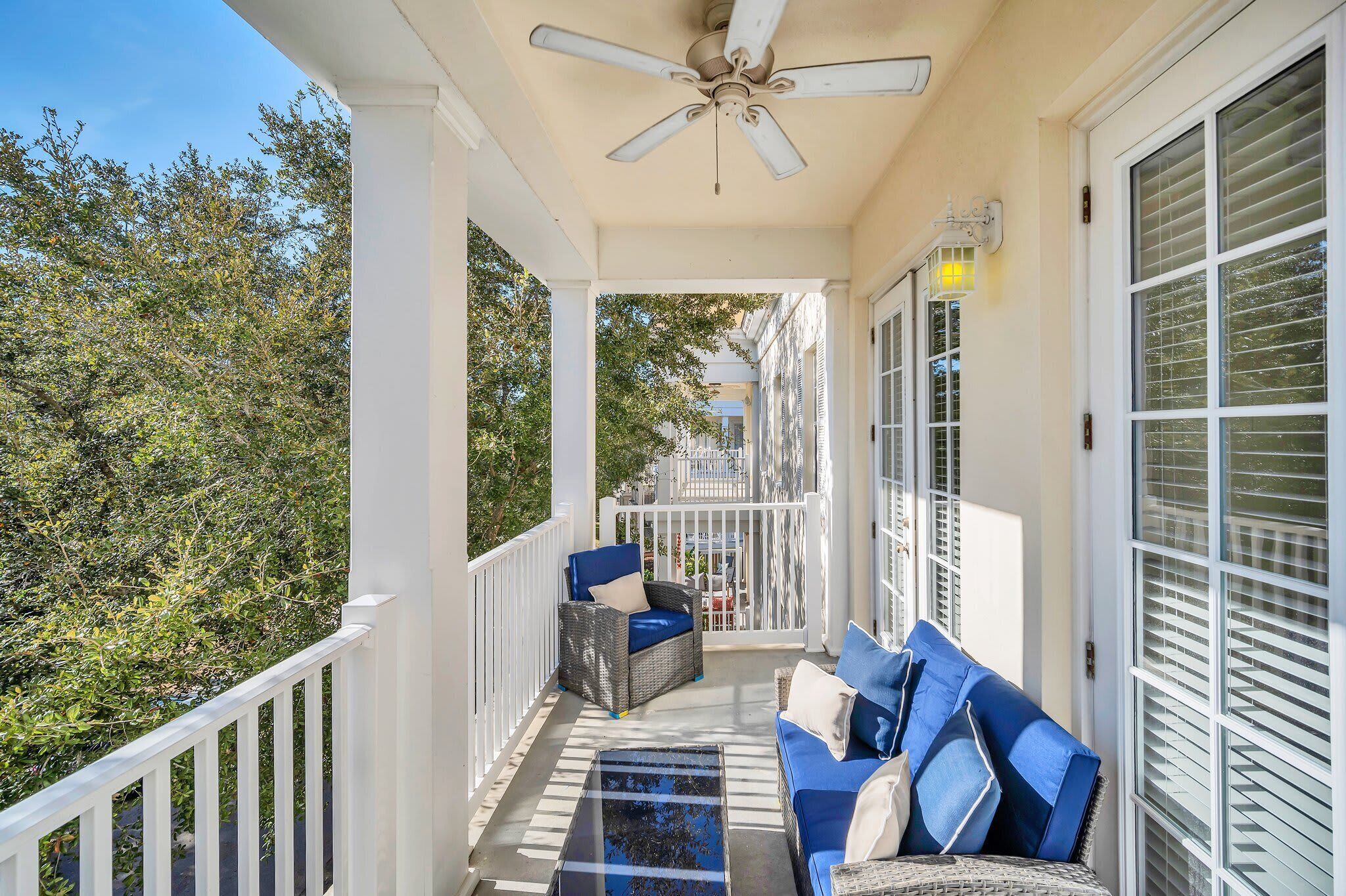 A covered porch with a ceiling fan, white railings, and a view of trees.