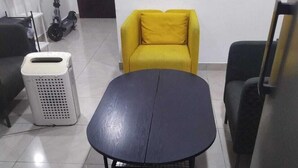A room with a round table, a yellow armchair, a white air purifier, and a scooter. - Hassani (Dubai)