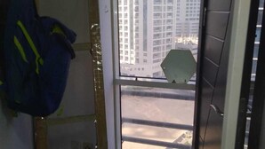 A room with a wooden ladder leaning against the wall, a window with a view of tall buildings, and a door with a dark panel. - Hassani (Dubai)
