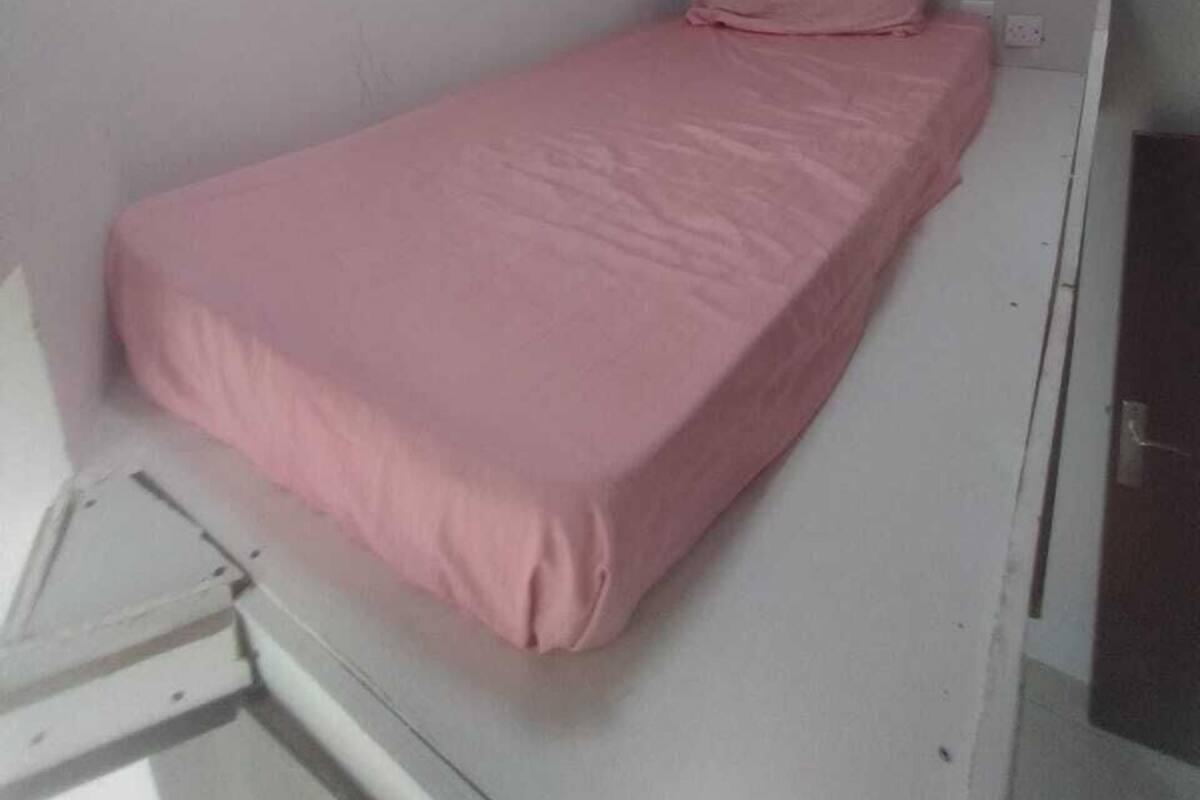 A small, single-bed room with a white bed and a pink bedspread.