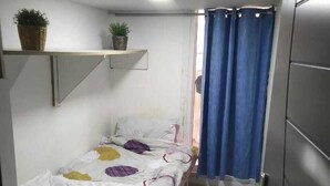A small, narrow room with a single bed, a shelf with plants, and a curtain. - Hassani (Dubai)