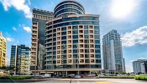 A modern multi-story building with a curved facade, surrounded by other high-rise buildings. - Hassani (Dubai)