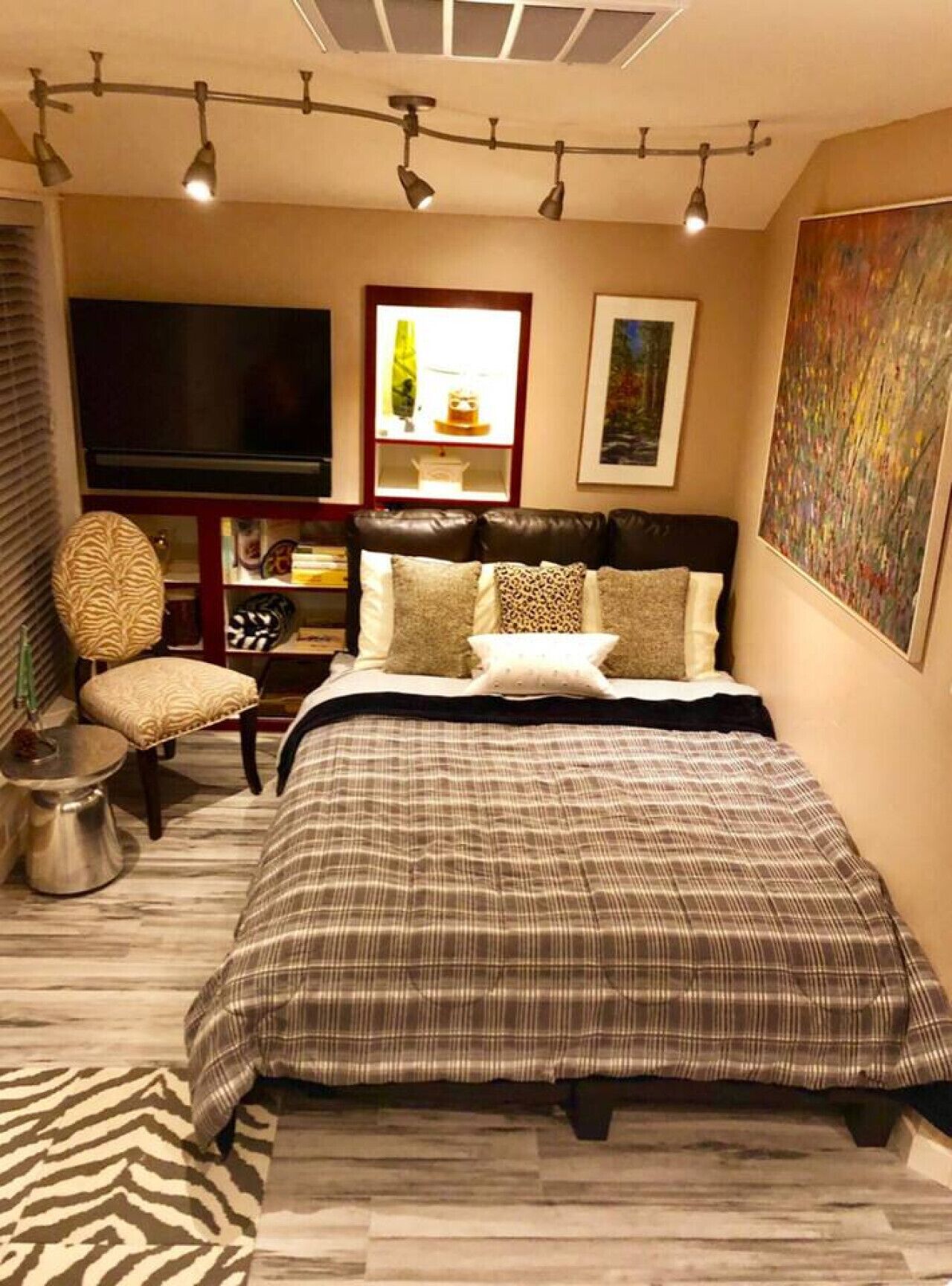 A bedroom with a large bed, a TV, a bookshelf, and a painting on the wall.