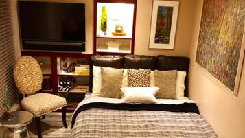 A bedroom with a large bed, a TV, a bookshelf, and a painting on the wall.