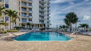 Une piscine avec des chaises longues, des palmiers et un immeuble à plusieurs étages doté de balcons.