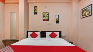 Een hotelkamer met een bed, rode en witte beddengoed, een nachtkastje, een spiegel en drie ingelijste kunstwerken aan de muur.