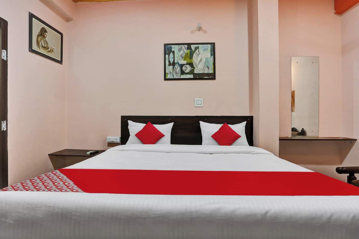 Un lit bien fait, recouvert d’une couvre-lit rouge et blanche, avec une tête de lit en bois et deux tables de chevet dotées de lampes.